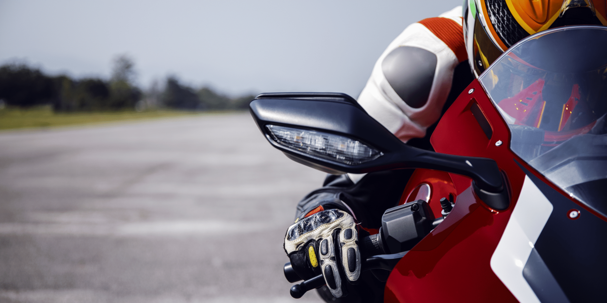Nahaufnahme eines Motorradfahrers in Schutzkleidung und Helm auf einem roten Sportmotorrad. Im Fokus steht der rechte Lenkergriff mit Spiegel und Handschuh.