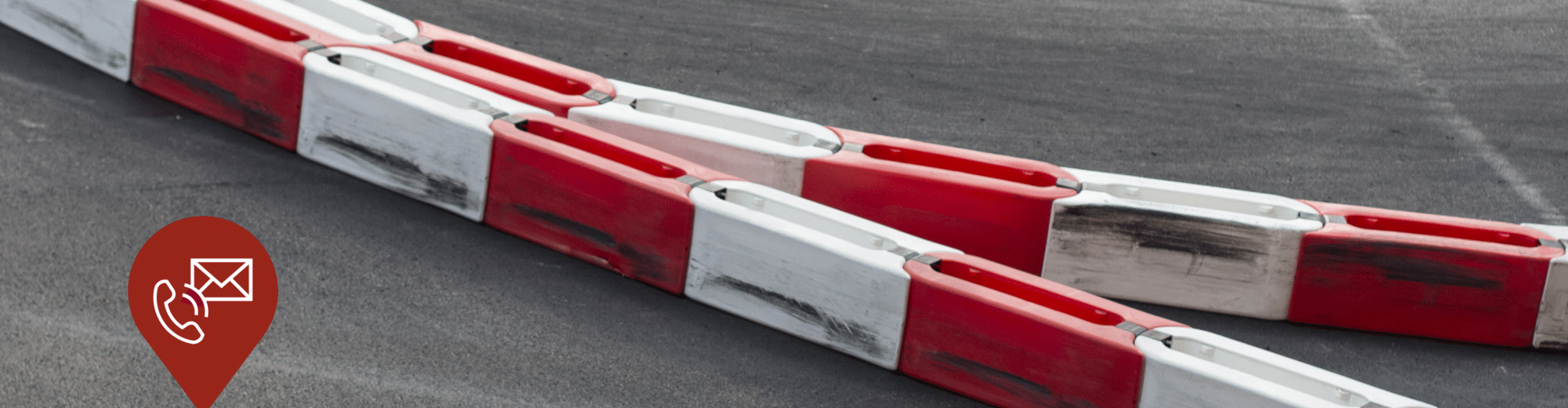 Rote und weiße Kunststoffbegrenzungen auf einer Kart- oder Rennstrecke. Links im Bild befindet sich ein Icon mit Telefon- und E-Mail-Symbol auf einem roten Marker.