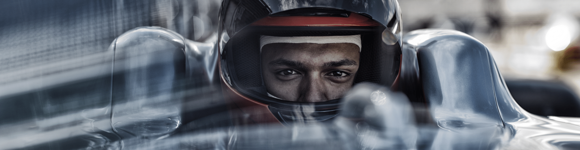 Nahaufnahme eines Rennfahrers mit Helm im Cockpit eines Formelwagens. Der Blick des Fahrers ist konzentriert und direkt nach vorn gerichtet.
